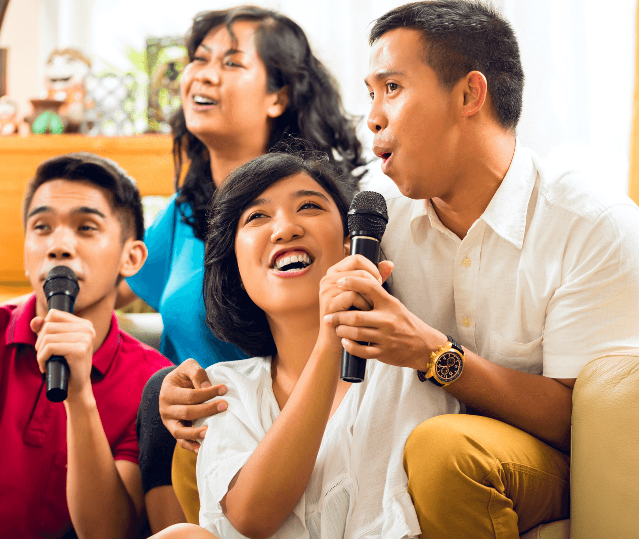 Friends sitting together on a couch singing karaoke with microphones.